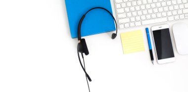 VoIP kulaklık, dizüstü bilgisayar klavyesinde kalem ve defter. Çağrı merkezi ve müşteri hizmetleri yardım masası için iletişim desteği. Beyaz arka planda izole edilmiş. Üst görünüm düz arkaplan. Metin tasarımı için boşluk