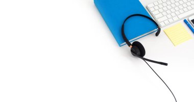 VoIP kulaklık, dizüstü bilgisayar klavyesinde kalem ve defter. Çağrı merkezi ve müşteri hizmetleri yardım masası için iletişim desteği. Beyaz arka planda izole edilmiş. Üst görünüm düz arkaplan. Metin tasarımı için boşluk