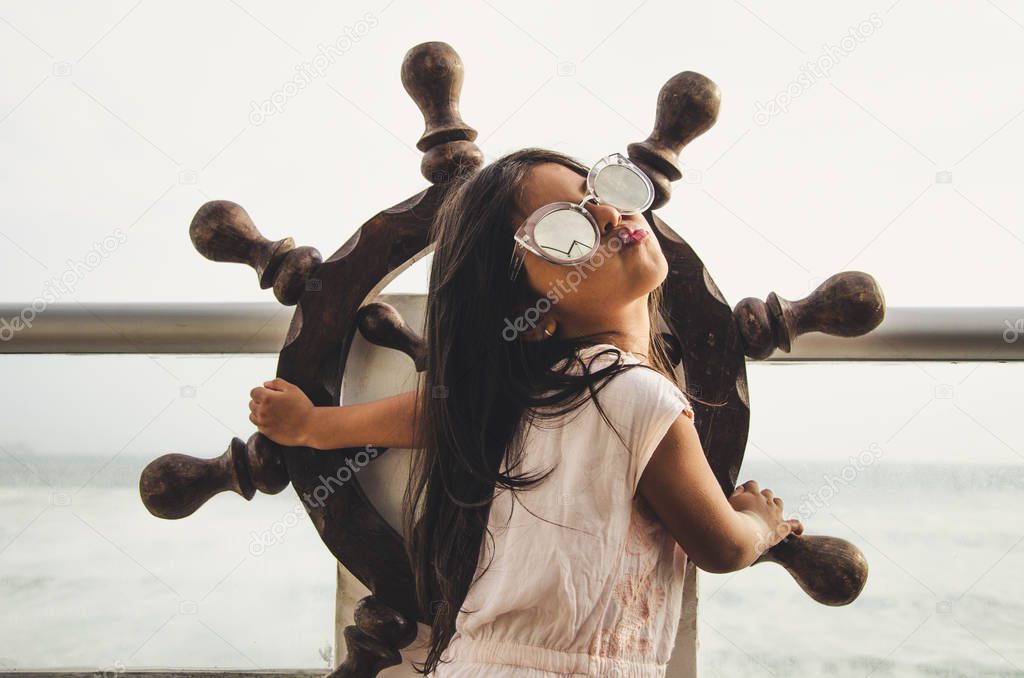 Little girl playing to be a sailor on a balcony with a boat rudder