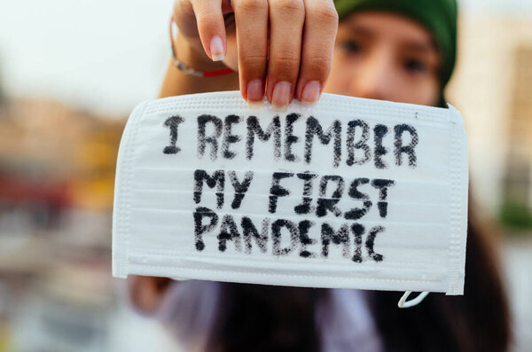 Девочка, молодая женщина в защитной стерильной медицинской маске на лице смотрит в камеру на улице, на азиатской улице показывает ладонь, руку, не останавливаясь. Загрязнение воздуха, вирус, китайская пандемия коронавируса
.