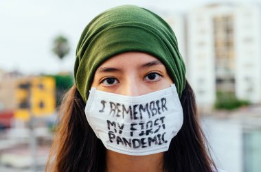 Kız, yüzünde koruyucu steril tıbbi maske takan genç bir kadın Asya sokak gösterilerinde, avuçlarında, ellerinde kameralara bakıyor. Hava kirliliği, virüs, Çin salgını koronavirüs konsepti.