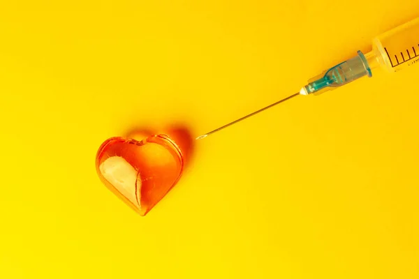Orangefarbener Hintergrund, auf dem Dekorationen in Herzform und medizinische Nadel zu sehen sind — Stockfoto
