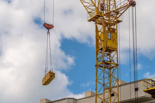 Tower crane yellow takes the building materials to the construction of multi-storey house, summer day — Stock Photo, Image