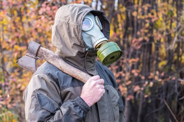 Man in gas mask with an axe standing on a background of autumn leaves, ready for a gas attack — Stock Photo, Image