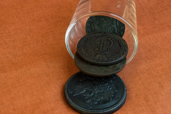 De un vaso de vidrio, las monedas viejas se vierten sobre un paño naranja — Foto de Stock