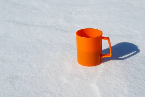 Orange plastic mug with a handle for tea in the snow, warm and cold — стоковое фото