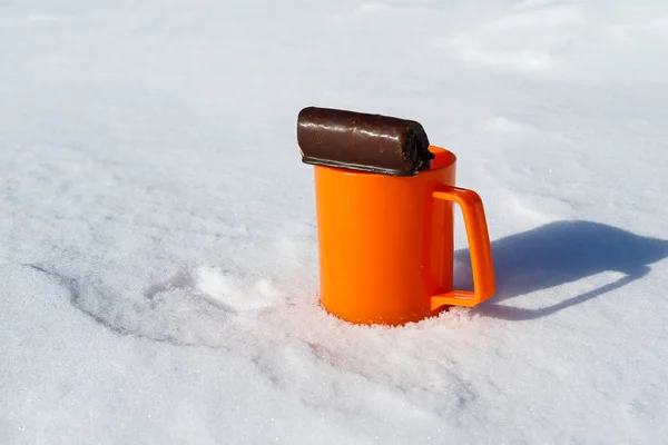 Шоколадное печенье и оранжевая кружка на снегу на холоде, на открытом воздухе — стоковое фото
