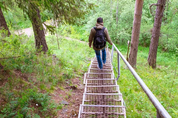 A traveler with a backpack goes down the stairs in a natural Park among the trees — Stock Photo, Image