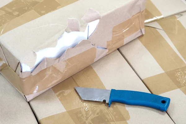 Embalagem danificada na caixa e uma faca com uma alça azul — Fotografia de Stock