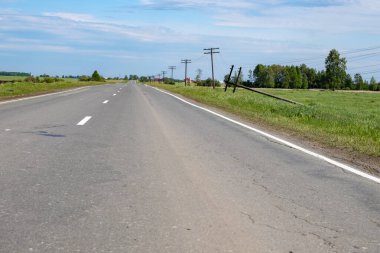 Yol kenarına uzanan asfalt yolda otlar ve direklerden biri düştü.