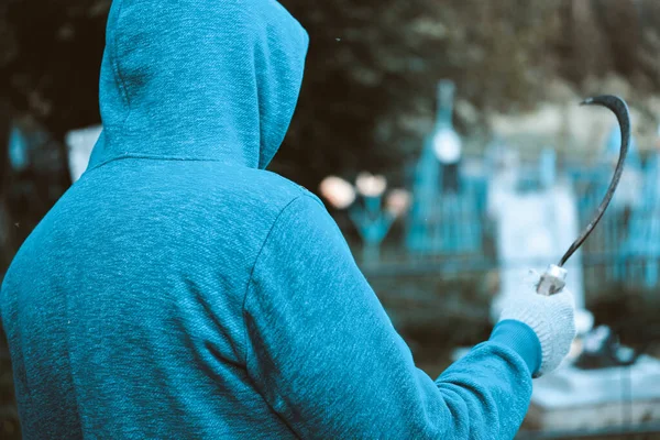 The man in whose hand is a sickle in the cemetery frightening photo view from the back — Stock Photo, Image