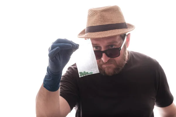 Un uomo con la barba in un cappello sulle mani indossando guanti di gomma esamina un pacchetto di pillole — Foto Stock