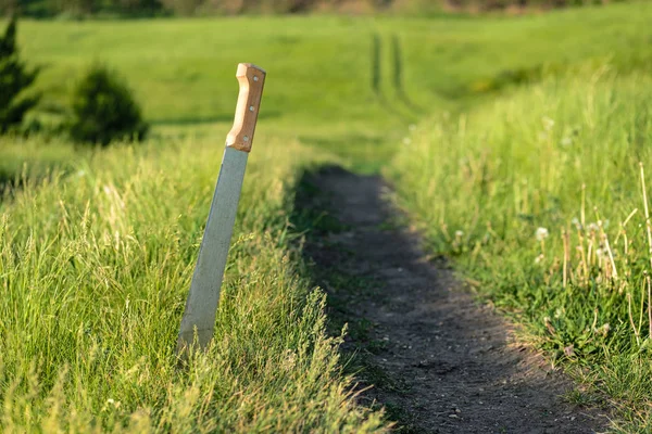 Une épée coincée dans le sol à côté d'une route de campagne — Photo