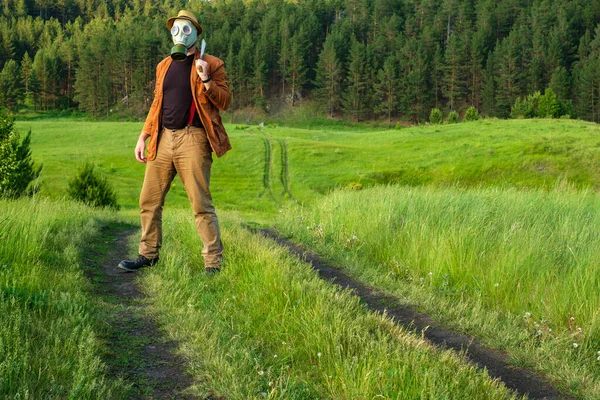 Sur la route est un homme sur son épaule il a une épée sur son visage un masque à gaz sur sa tête un fond de chapeau herbe d'été juteuse et brillante — Photo