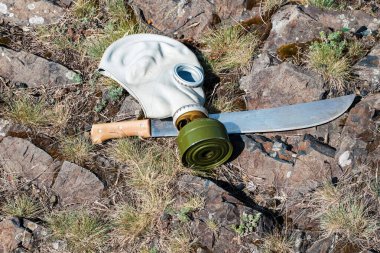 Eski tip lastik gaz maskesi ve çimlerin üzerinde duran kılıç palası.