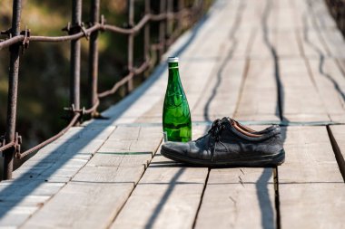 bottle on the suspension bridge and next boots are old worn clipart
