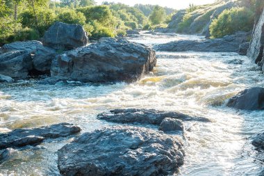 Arkaplanda taşların arasında akan hızlı bir derede bir dağ nehrinin suları.