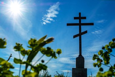 Ortodoks haçı üzerinde çimlerin altından soldaki mavi gökyüzüne bakan güneş ışıl ışıl parlıyor.