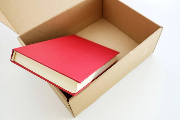 In an open box, a book sticks out from under the parcel — Stock Photo, Image