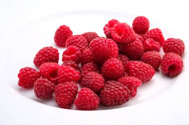 Büyük beyaz bir tabakta olgun kırmızı ahududu. Bir sürü böğürtlen gelişigüzel serilmiş.