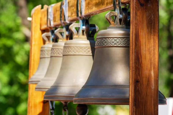 Vier Glocken Hängen Einem Holzrahmen Auf Dem Hintergrund Der Straßenbäume — Stockfoto