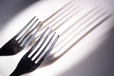Beyaz seramik bir yüzeydeki iki çatalın dişlerindeki uzun gölgelerin soyutlanması. Kontrastlı ışıkta çatal bıçak takımı
