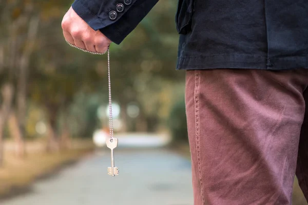 a key hanging on a chain in a man\'s hand against the blurred background of a summer trail in the Park