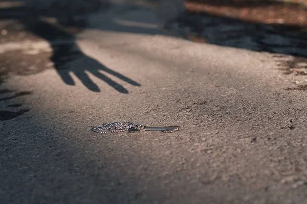 手的影子伸向沥青路面上的钥匙 鬼找到了钥匙 这是一种神秘的情况 — 图库照片