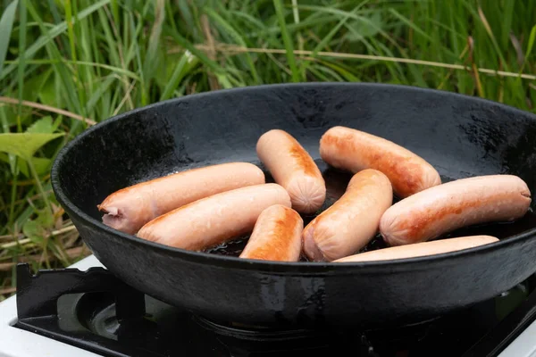 sausages in a frying pan during a summer picnic in nature. lunch during outdoor recreation