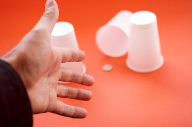 El yüksük oyununu kazanmak için uzanır. Adam hangi bardakta plastik ödül olduğunu tahmin etti.