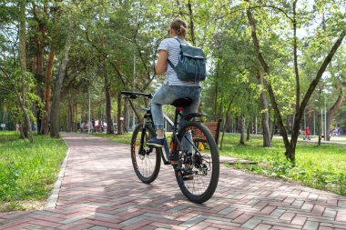 Rusya, Kamensk Uralsky, 10 Ağustos 2019. Sırtında sırt çantası olan bir kız bisiklet parkında bisiklet sürüyor.