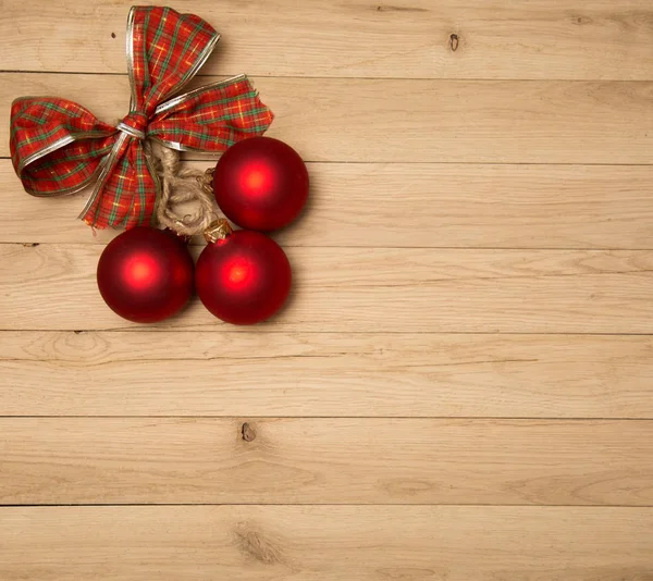 Drie rode kerstballen en een strik op een eiken board — Stockfoto