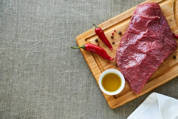 Piece of raw beef with spices and oil on a wooden cutting board