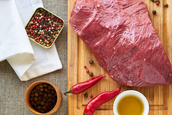 Piece of raw beef with spices and oil on a wooden cutting board