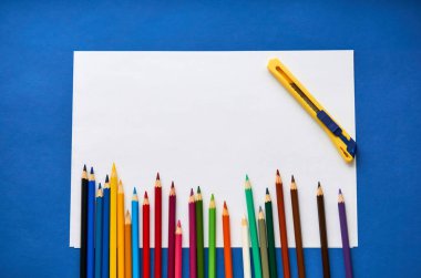 Mavi arkaplanda renkli kalemler ve beyaz kağıt.                               