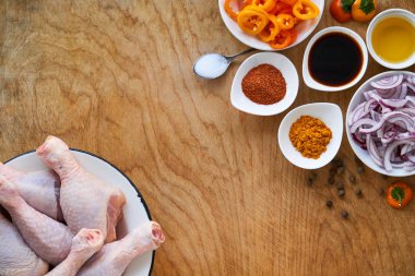 Çiğ tavuk budu, sebze ve baharatla ahşap bir arka planda.                                