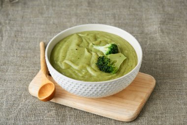 Tekstil arka planında beyaz bir kâsede brokoli kremalı çorba.                                