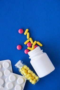 Mavi arka planda şişedeki çeşitli renkli haplar.                                