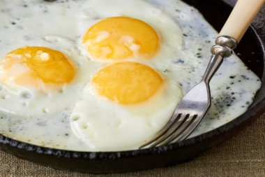 Tekstil arka planında dökme demir bir tavada kızarmış yumurta.                               