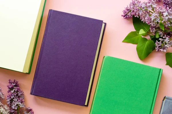 Flat lay of books with lilac branches on a pink background