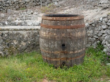 Taştan bir duvar yakınındaki bir çayır üzerinde eski şarap varil duran