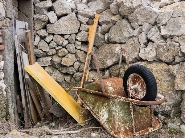 Alte rostige Schubkarre liegt auf dem Boden vor Steinmauer — Stockfoto