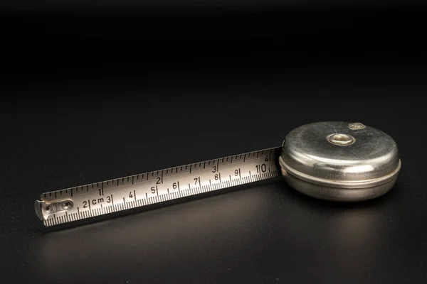 An old measuring tape made of steel lying on a black background — Stock Photo, Image