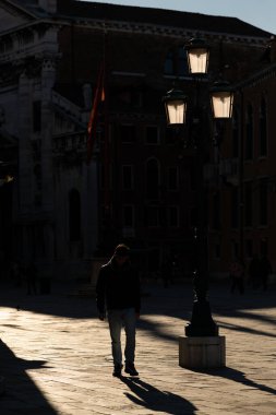 Venedik / İtalya - 02 / 03 / 2020: Venedik 'te (İtalya) bir sokakta yürüyen bir adamın silüeti, güneş gören bir sokak lambası