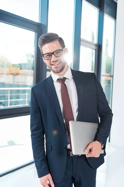 Businessman holding laptop in office — Free Stock Photo