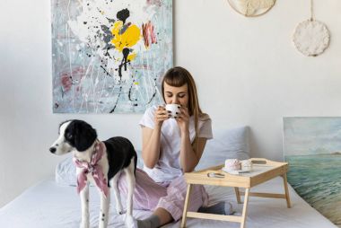köpek yavrusu ile birlikte yatakta istirahat ederken kahve içme kadın