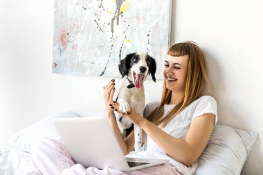 portrait of happy woman playing with puppy in morning at home clipart