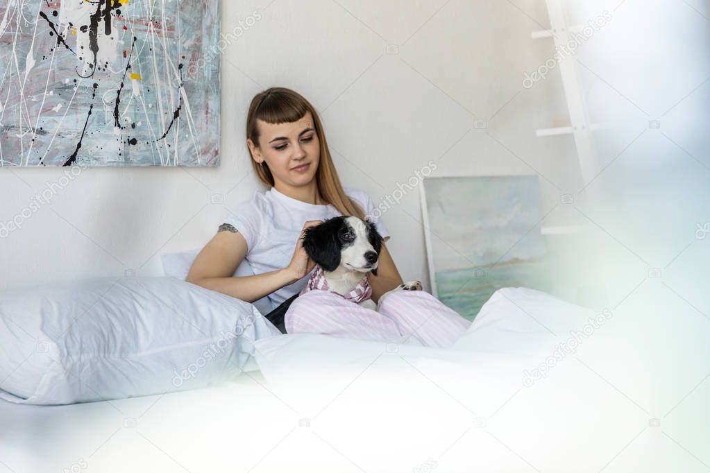 portrait of young woman with little puppy resting in bed in morning at home