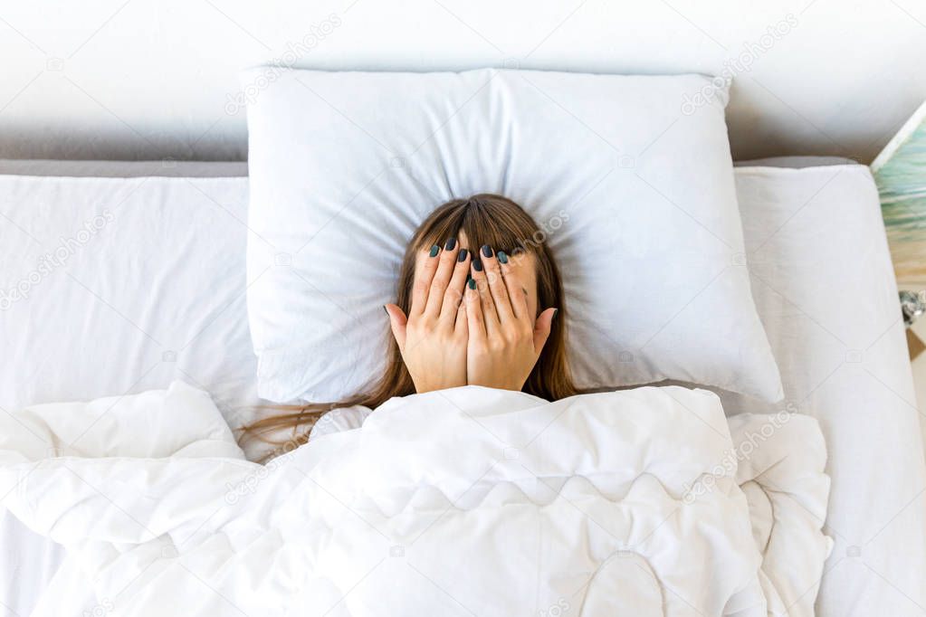 obscured view of woman covering face with hands while lying in bed