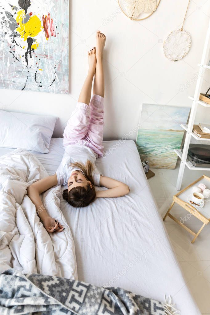 young woman in pajamas resting on bed in morning at home